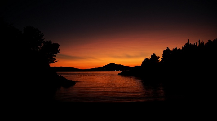 Sunset over the water with silhouetted trees and hills