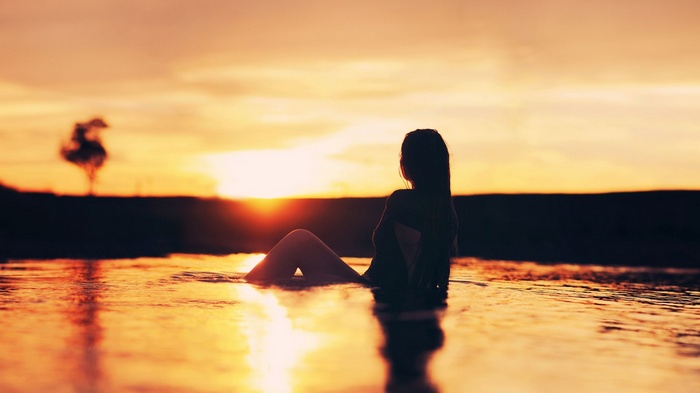 Woman sitting in water at sunset