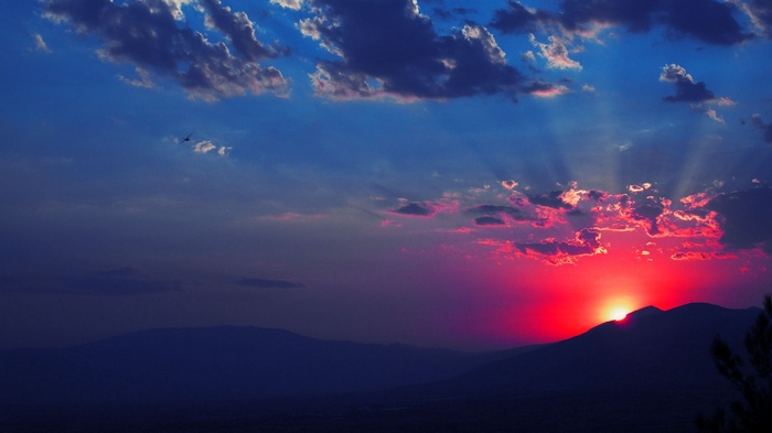 Sunset over mountains with sun rays and clouds