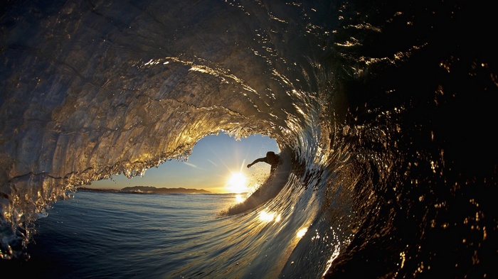 Surfer rides a wave at sunset through a heart-shaped opening