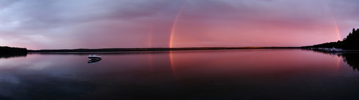Lake with boat and double rainbow at sunset
