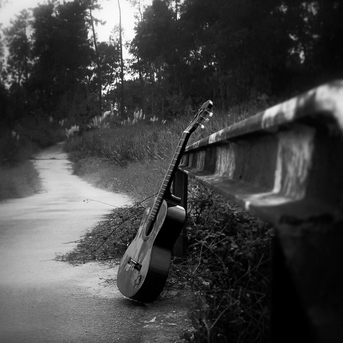 Acoustic guitar leaning on a guardrail by a path