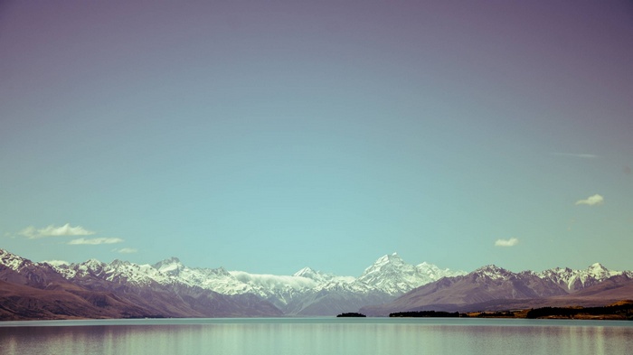 Snow-capped mountains reflected in a calm lake under a clear sky