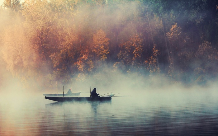 Fishermen in boats on a misty lake at sunrise