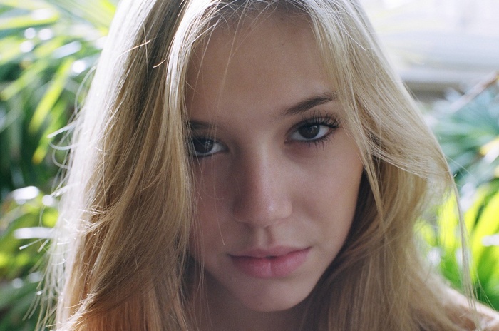 Alexis Ren portrait with blonde hair and green foliage