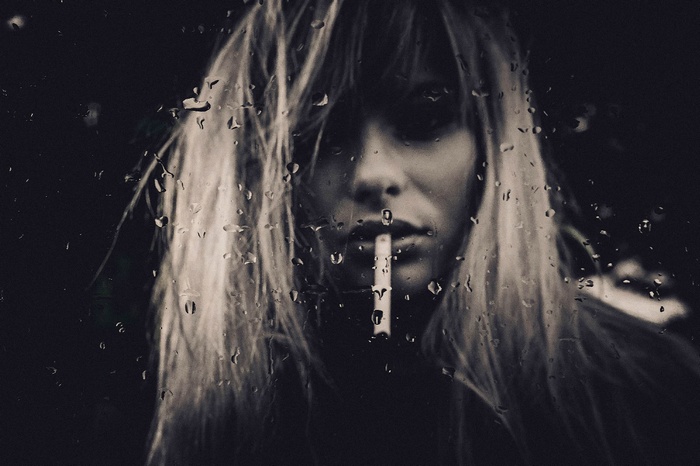 Woman smoking through a wet glass window