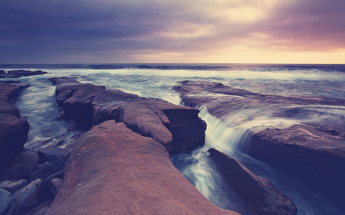 Ocean waves crashing on rocky shore at sunset