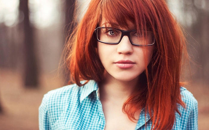 Young woman with red hair and glasses in a blue shirt