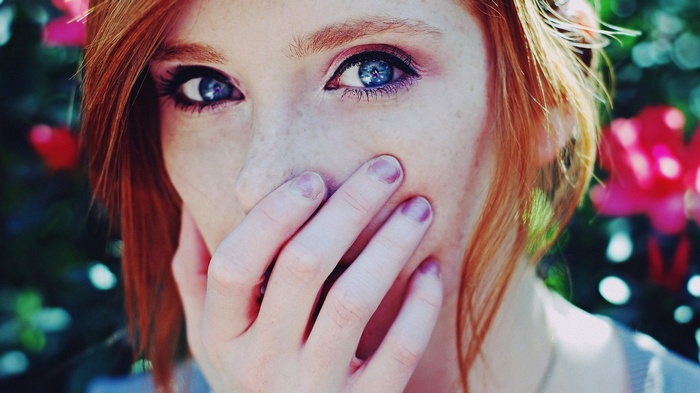 Woman with red hair and blue eyes covering her mouth
