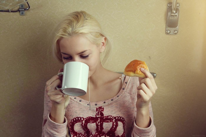 Blonde woman drinking tea and holding a bun