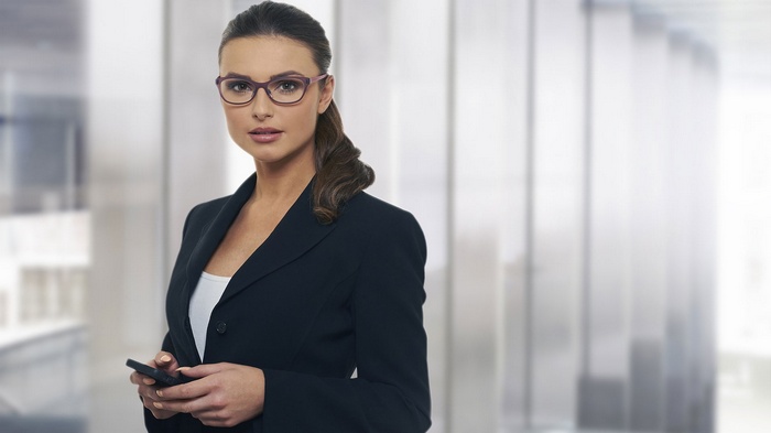 Woman in a suit wearing glasses holding a phone