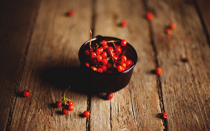 Red berries in a bowl on a wooden surface