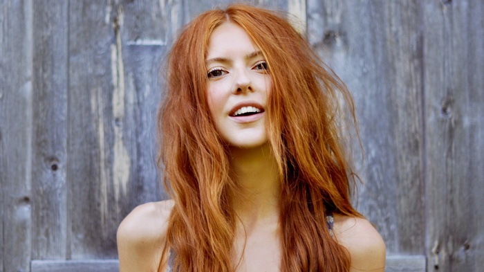 Redhead woman with long curly hair in front of wooden surface