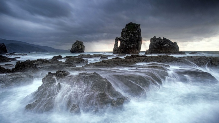 Stormy ocean waves crash against rocky shore with sea stacks