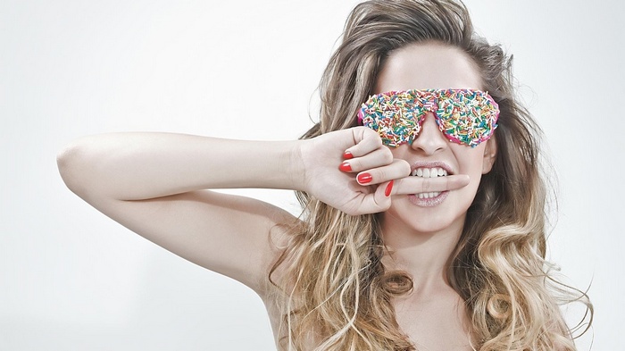 Woman with sprinkles-covered sunglasses biting finger