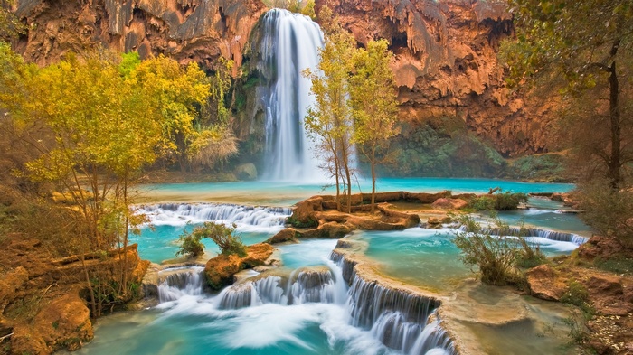Waterfall cascading into turquoise pools surrounded by autumn foliage