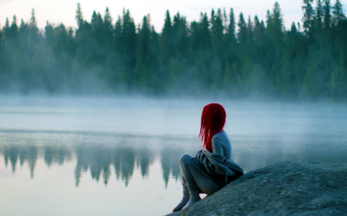 Woman with red hair sitting by a misty lake