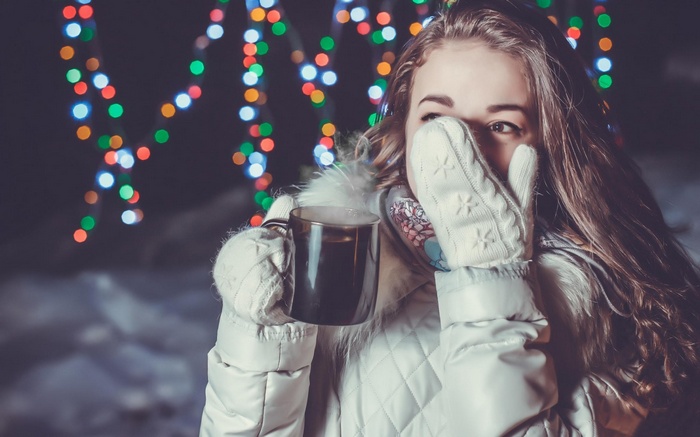 Woman in white jacket holding a cup with Christmas lights