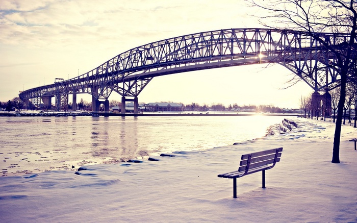Winter bridge over a frozen river with a bench