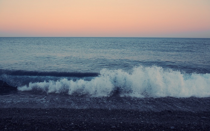 Ocean waves crashing on a pebble beach at sunset