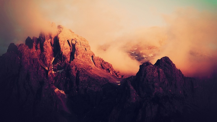 Jagged mountains shrouded in orange clouds at sunset
