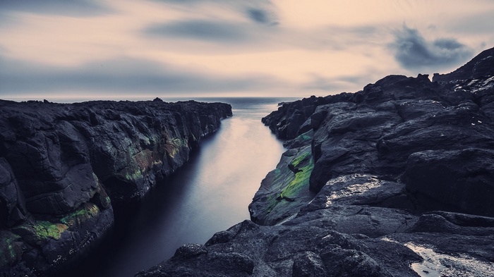 Dark rocky coast with a calm sea channel