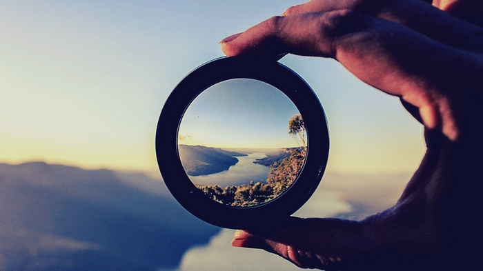 Hands holding a lens framing a scenic river valley