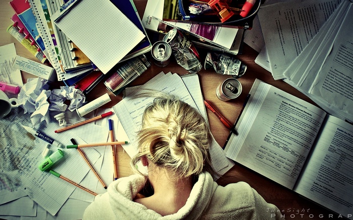 Tired blonde woman surrounded by study materials and cans