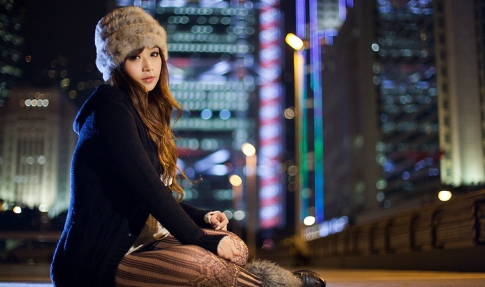 Woman in fur hat sitting in urban night setting