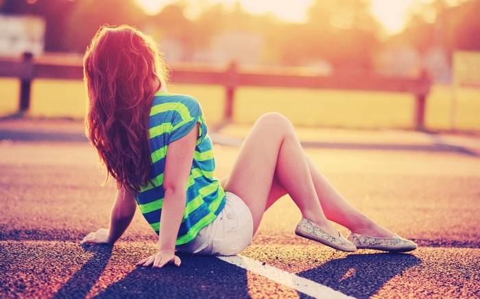 Woman with long wavy red hair sitting on asphalt