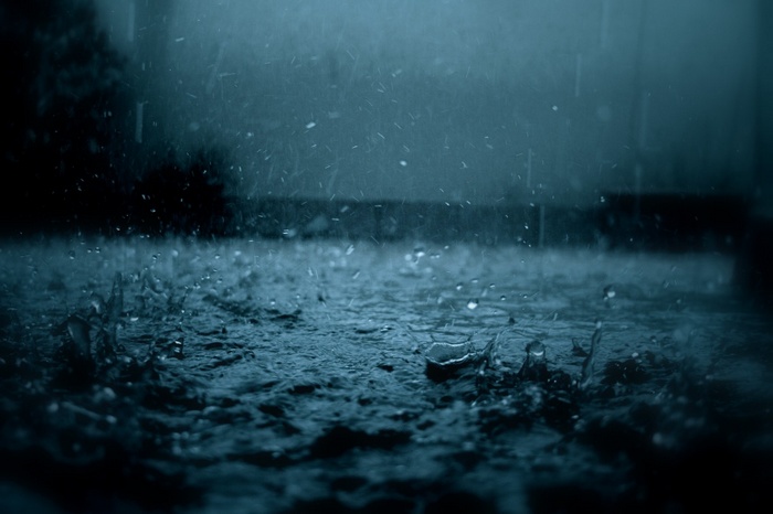 Raindrops falling on a dark, wet surface
