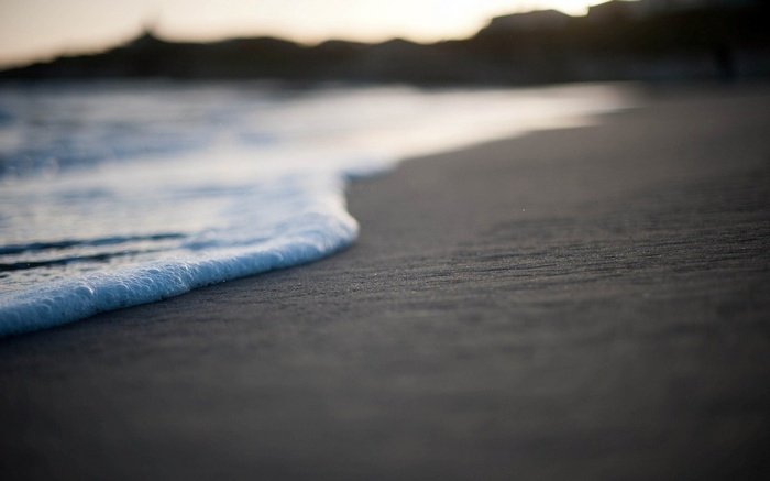 Gentle wave washes onto a sandy beach at sunset
