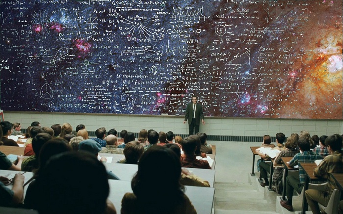 Professor lecturing students in front of a blackboard with space images and equations