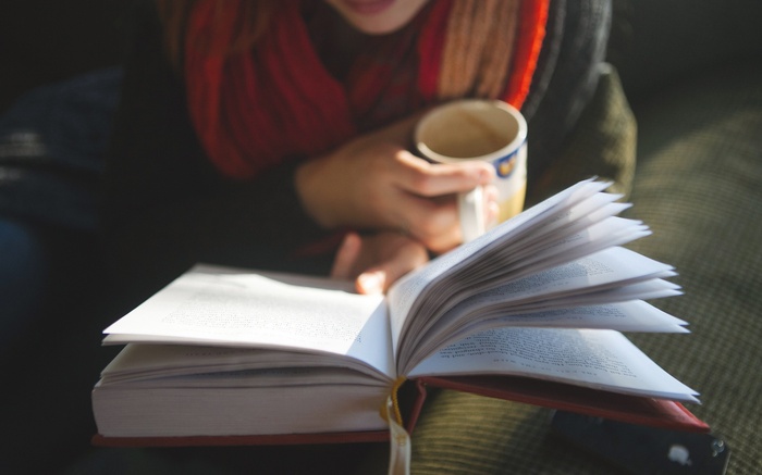 Person reading a book and holding a mug