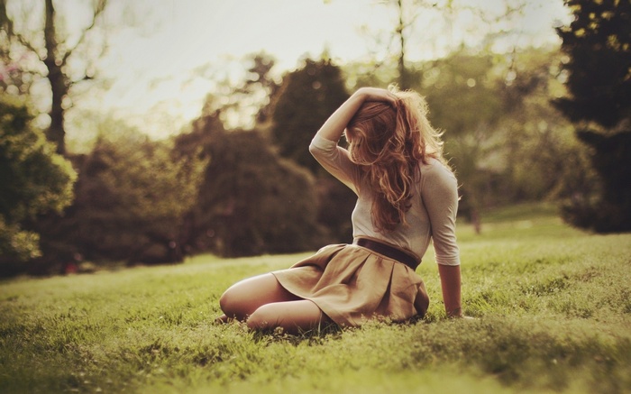 Woman with hands in hair sitting on grass outdoors
