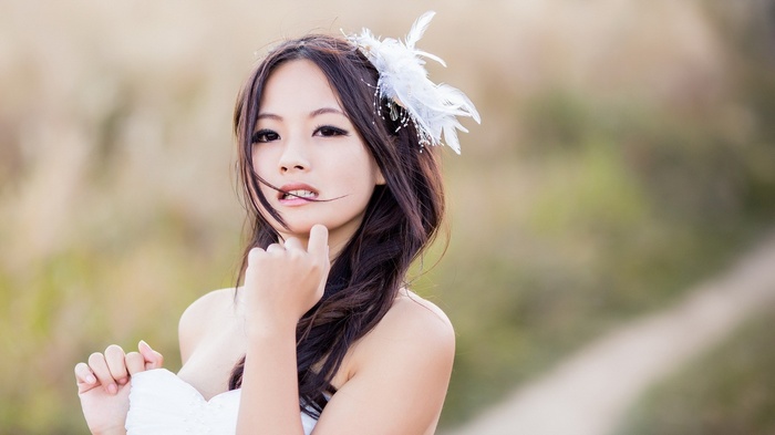Asian woman with white feather hair accessory in a white dress