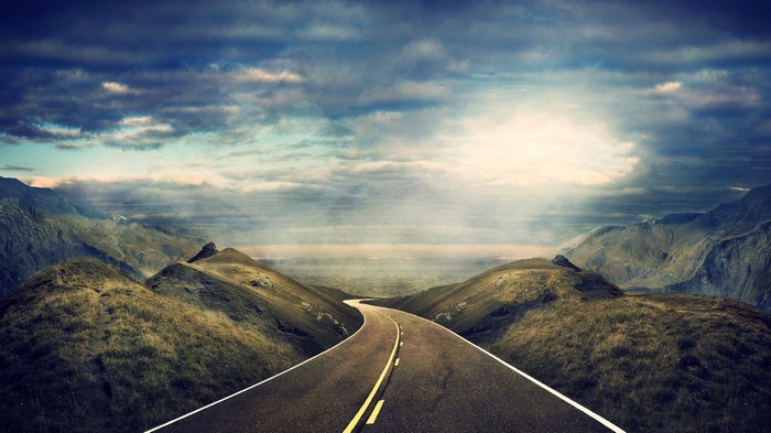 A winding road through mountainous landscape under a dramatic sky