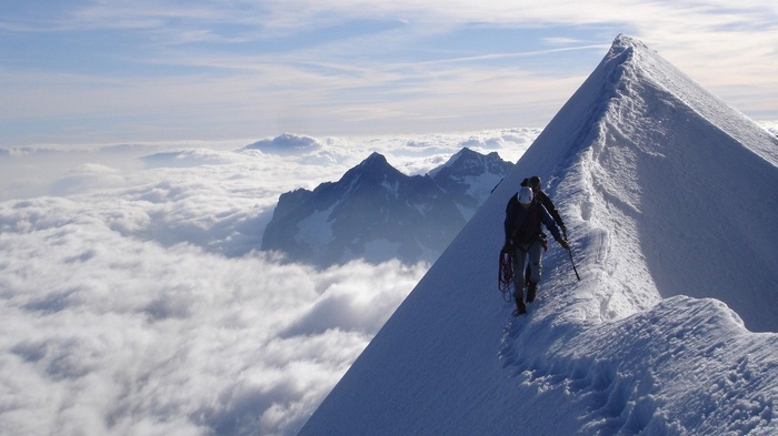 Climbers on a snowy mountain ridge above clouds
