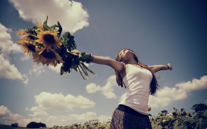 Woman holding sunflowers in a field under a cloudy sky