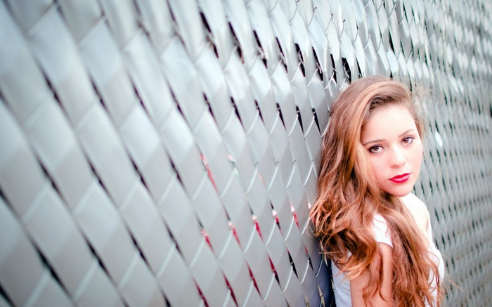 Woman with long hair and red lipstick leaning on a fence