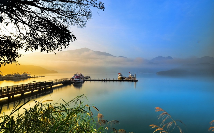Sunrise over a misty lake with boats docked at a pier