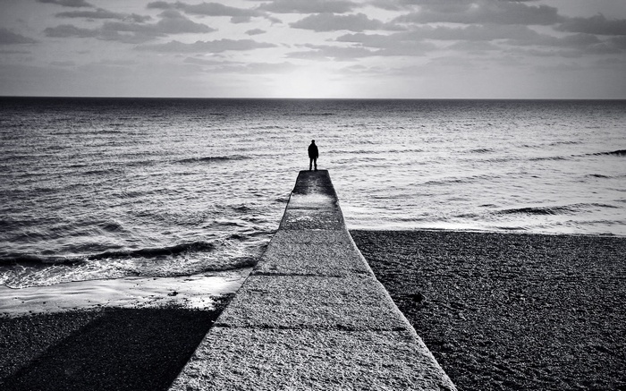 A lone figure stands on a pier overlooking the sea