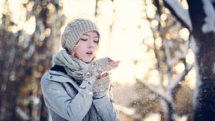 Woman in winter hat and scarf blowing snow