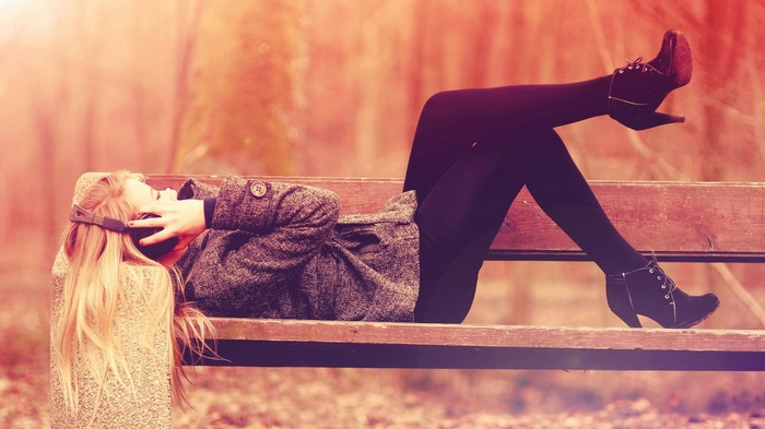 Woman with headphones lying on a park bench