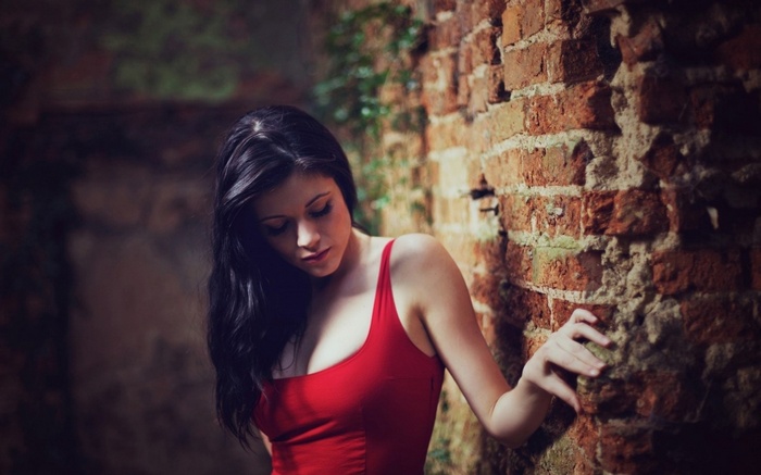 Woman in red dress leaning against a brick wall