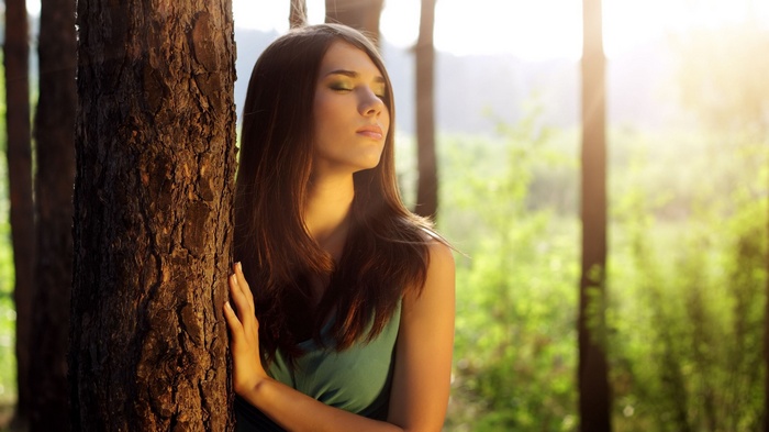 Woman with closed eyes leaning against a tree