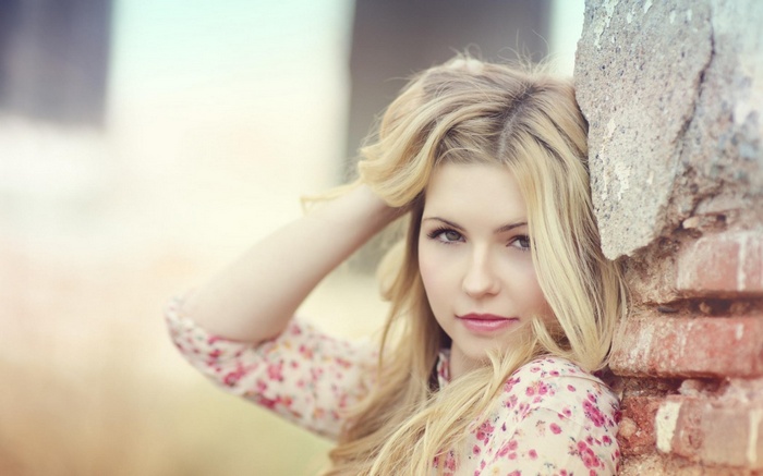 Woman with blonde hair leaning against a brick wall