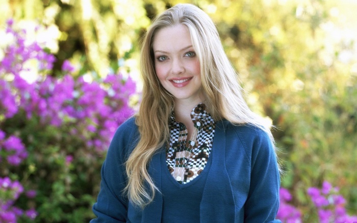 Amanda Seyfried smiling outdoors with purple flowers
