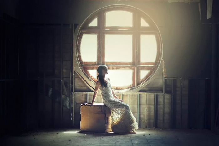 Woman in white dress sitting on box in front of circular window