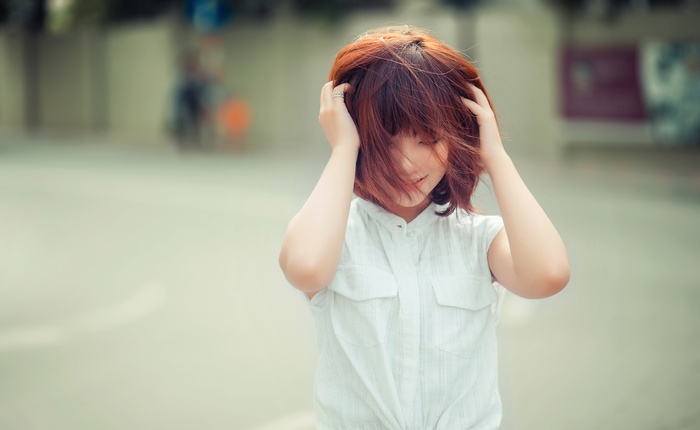 Asian woman with hands on head in white top